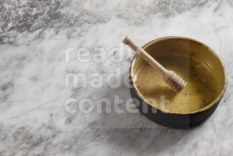 Multicolored pottery oven plate with wooden honey dipper in it on grey marble background