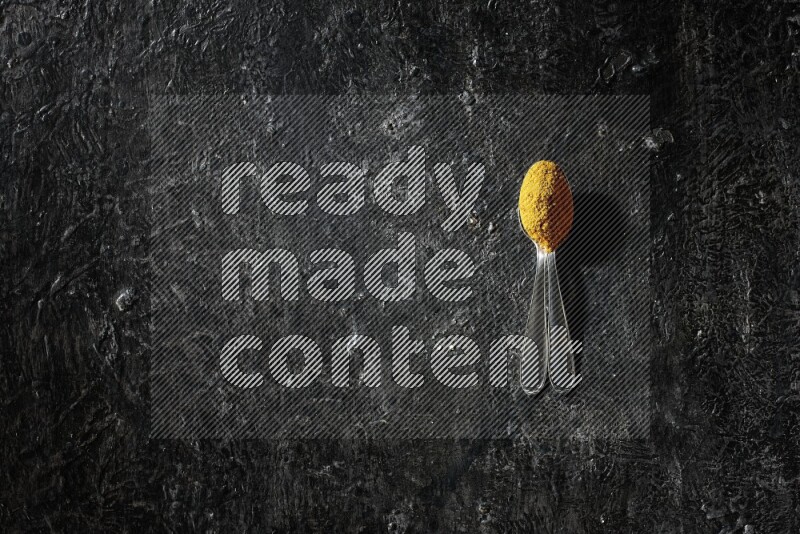 2 metal spoons full of turmeric powder on a textured black background