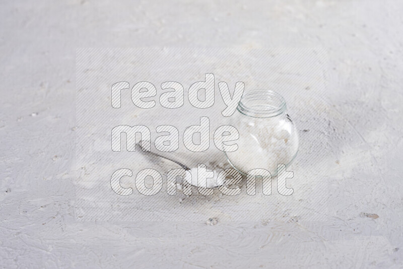 A glass jar full of coarse sea salt crystals on white background