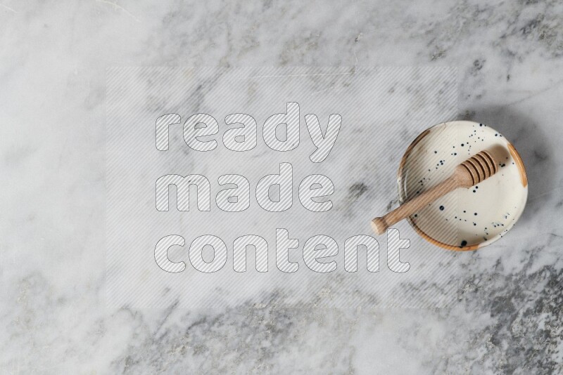 Multicolored pottery bowl with wooden honey dipper in it on grey marble background