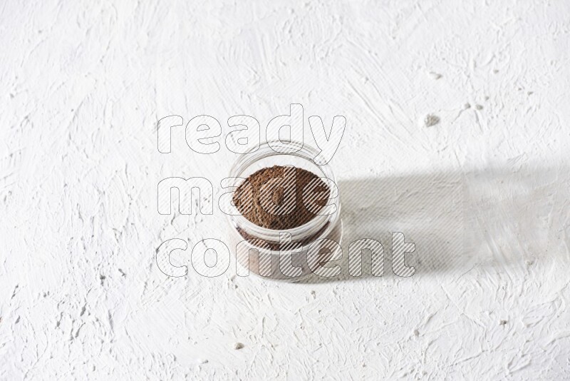 A glass jar full of cloves powder on a textured white flooring