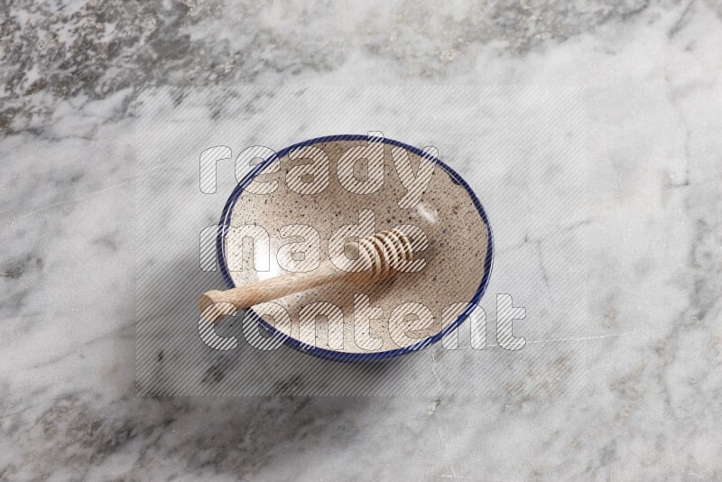 Multicolored pottery bowl with wooden honey dipper in it on grey marble background