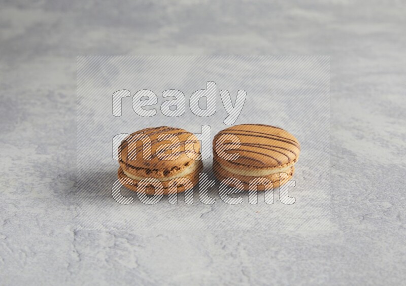 45º Shot of two light brown  Almond Cream macarons  on white  marble background