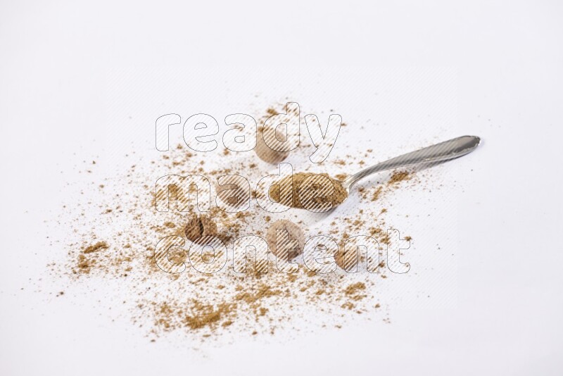 A metal spoon full of nutmeg powder with some of the powder and seeds beside it on a white flooring