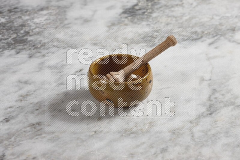 Multicolored pottery bowl with wooden honey dipper in it on grey marble background