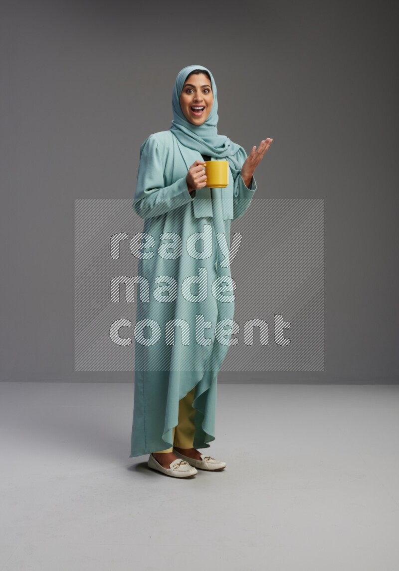 Saudi Woman wearing Abaya standing  holding a mug on Gray background