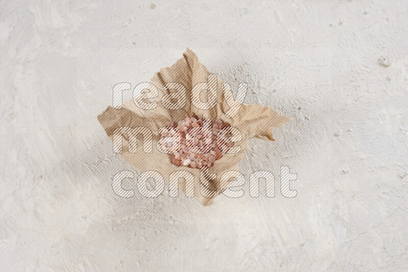 A crumpled piece of paper full of pink himalayan salt on white background