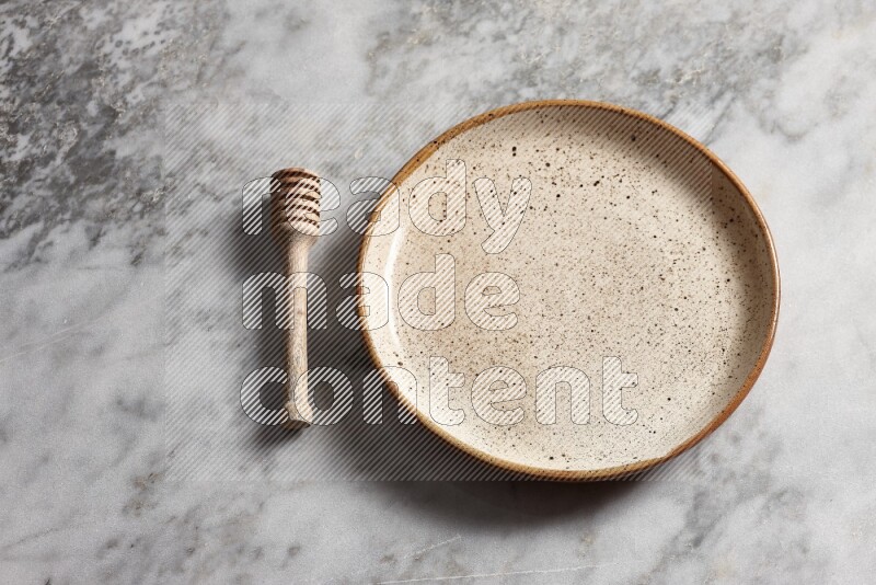 Multicolored pottery plate with wooden honey dipper on the side on grey marble background