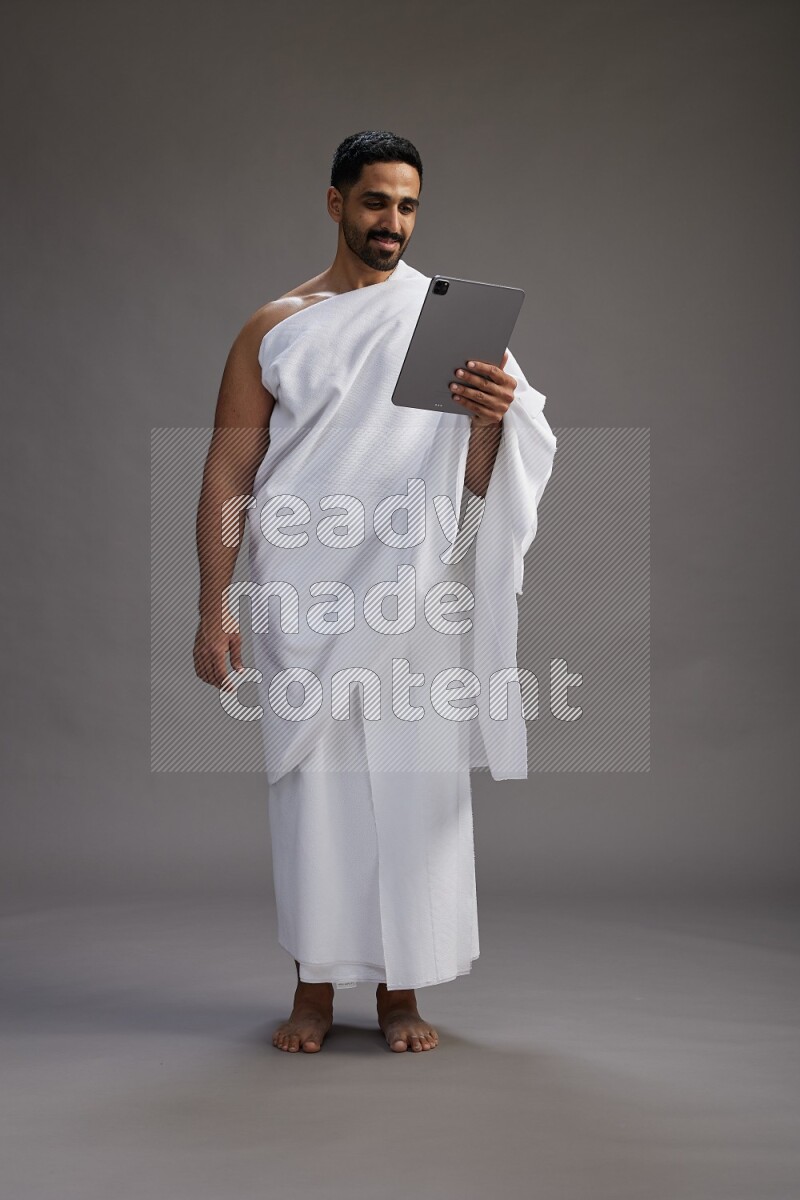 A man wearing Ehram and holding a tablet on gray background