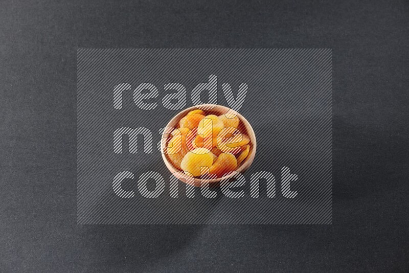 A wooden bowl full of dried apricots on a black background in different angles