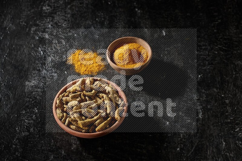 وعاءان خشبيان، أحدهما ممتلئ ببودرة الكركم والآخر بأصابع الكركم المجففة، على خلفية سوداء