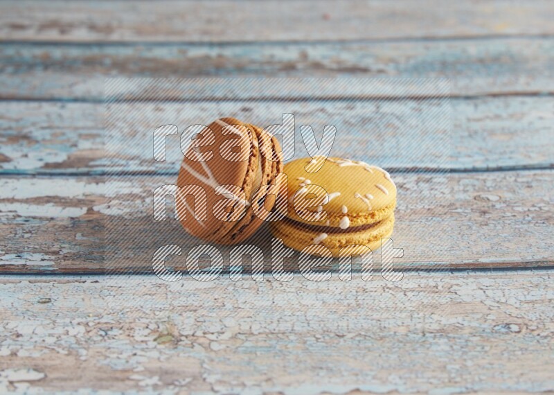 45º Shot of of two assorted Brown Irish Cream, and Yellow Piña Colada macarons on light blue background