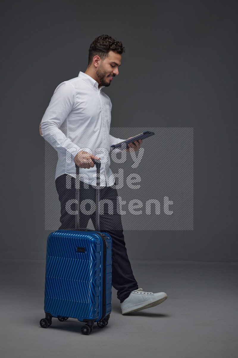 A man wearing smart casual with and pulling a carry-on luggage eye level on a gray background