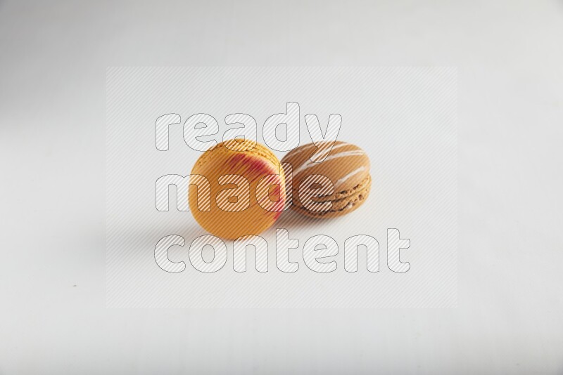 45º Shot of of two assorted Brown Irish Cream, and Orange Exotic macarons on white background