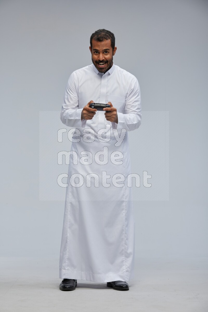 Saudi man Wearing thob standing holding joystick on Gray background