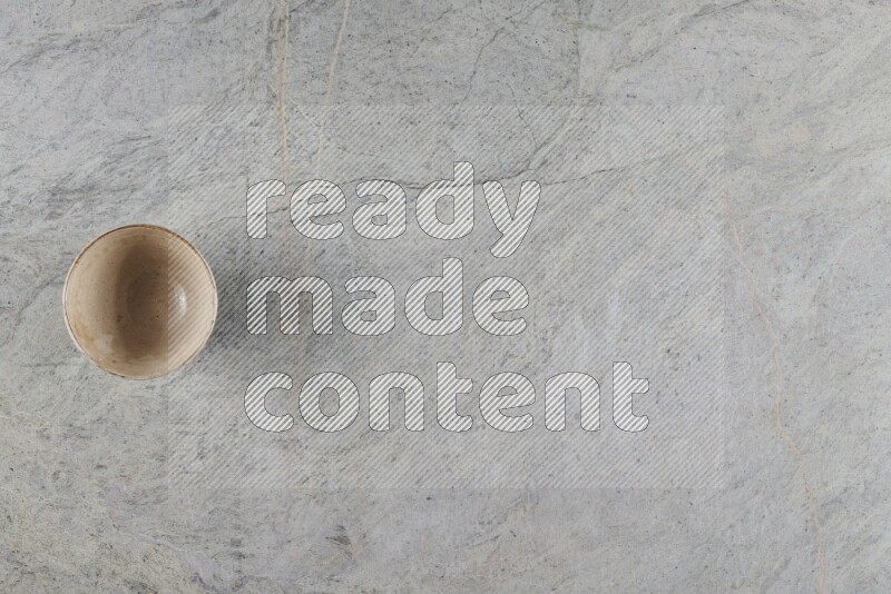 A small beige pottery bowl on grey marble background