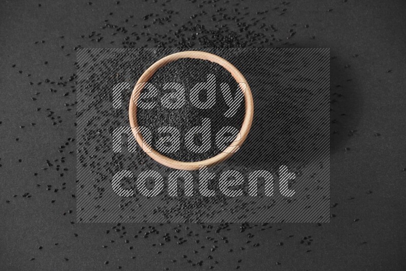 وعاء خشبي ممتلئ ببذور حبة البركة محاط ببعض البذور علي خلفية سوداء