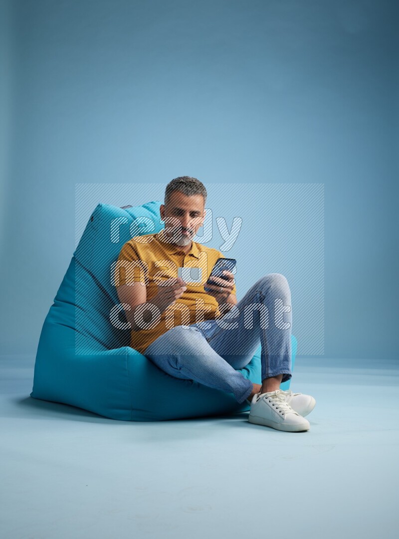 A man sitting on a blue beanbag and holding ATM card with phone
