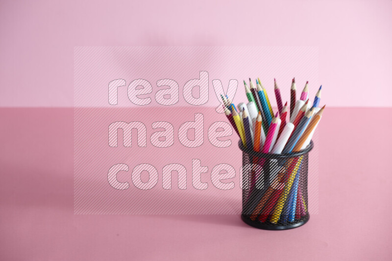 Pens, pencils and other different school supplies in a metal pen holder on rose background