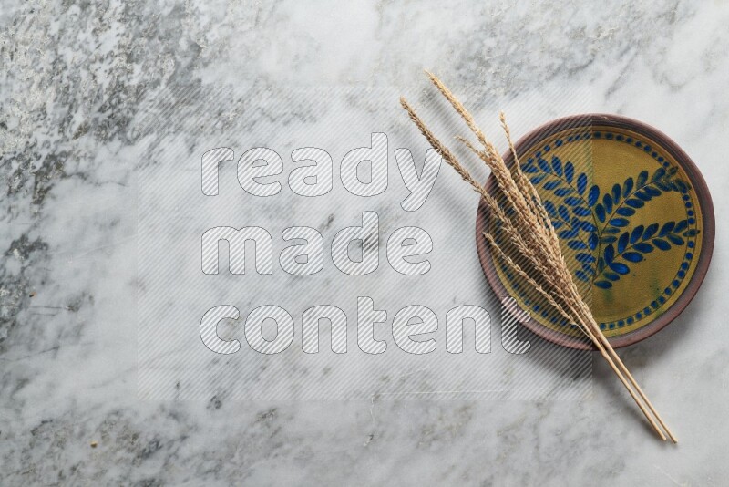 Wheat stalks on decorative pottery plate on grey marble background
