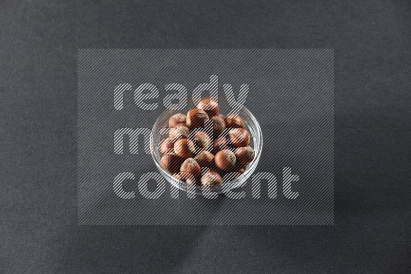 A glass bowl full of hazelnuts on a black background in different angles