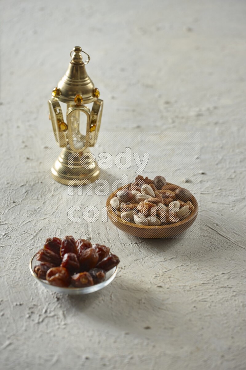 A golden lantern with different drinks, dates, nuts, prayer beads and quran on textured white background