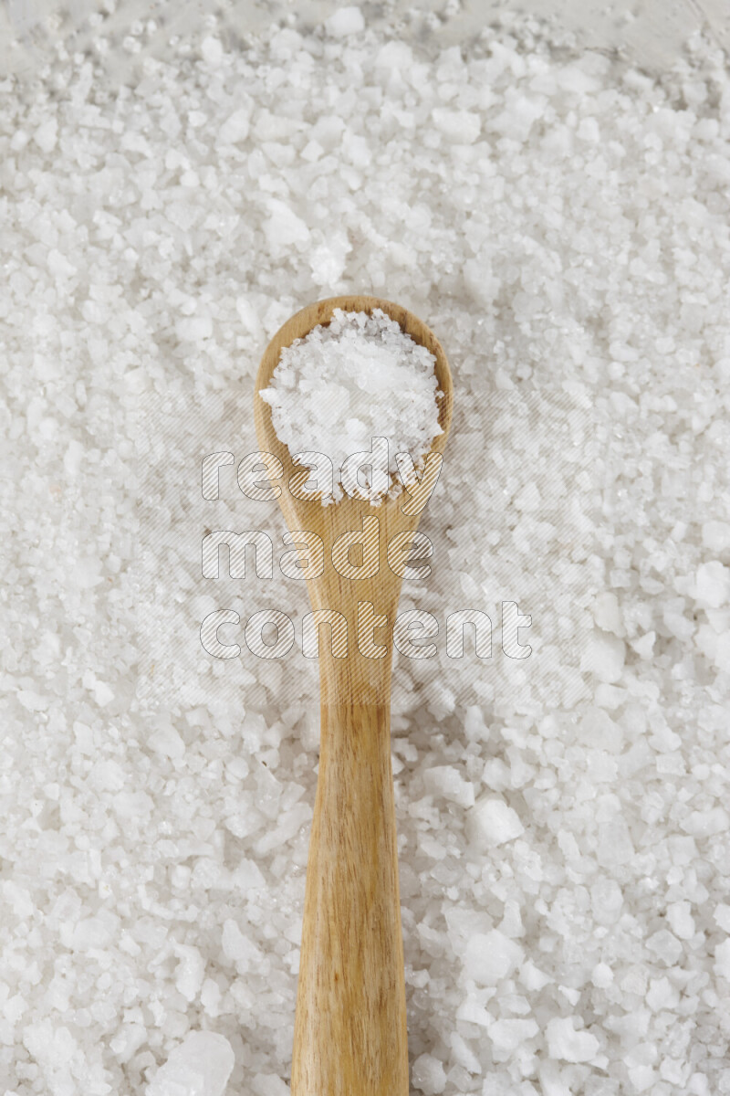 A wooden spoon full of white salt on white background