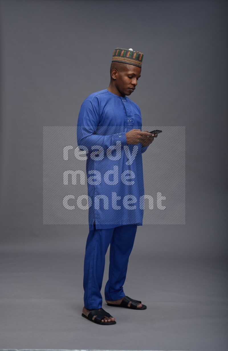 Man wearing Nigerian outfit standing texting on phone on gray background