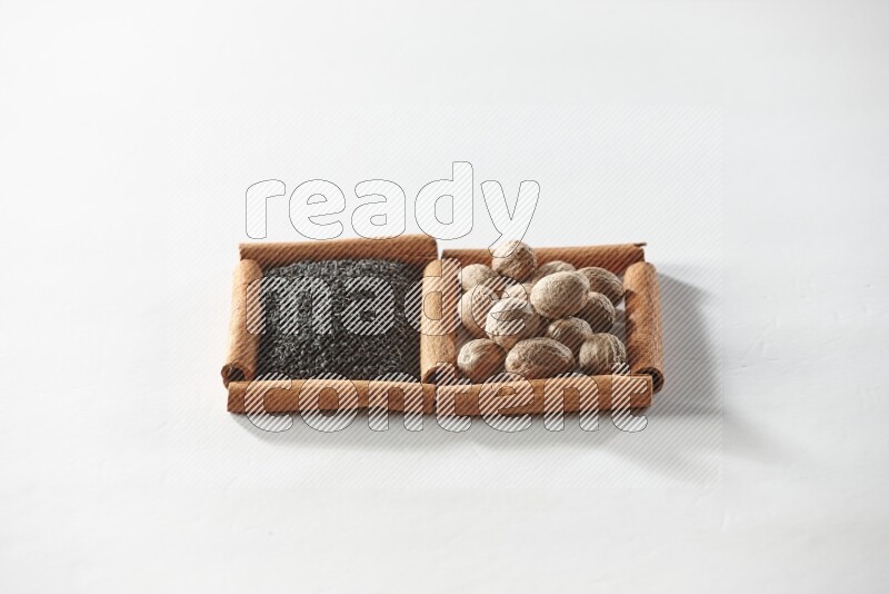 مربعان من أعواد القرفة ممتلئان بحبة البركة السوداء وجوزة الطيب علي خلفية بيضاء