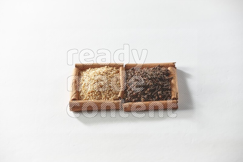 مربعان من أعواد القرفة ممتلئان بالقرنفل وبذور السمسم علي خلفية بيضاء