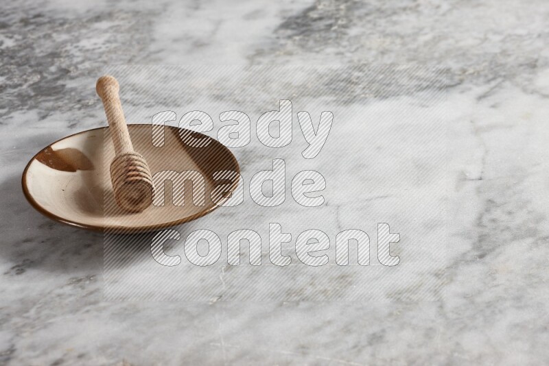 Multicolored pottery plate with wooden honey dipper in it on grey marble background