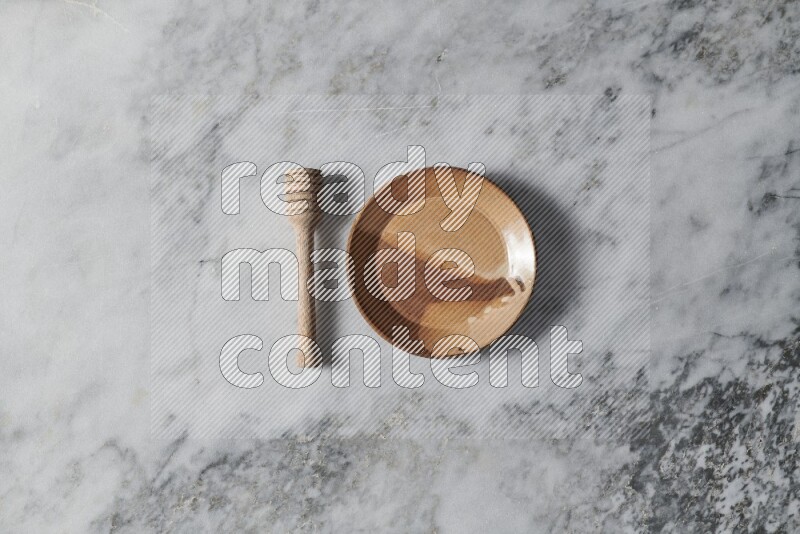 Multicolored pottery plate with wooden honey dipper on the side on grey marble background