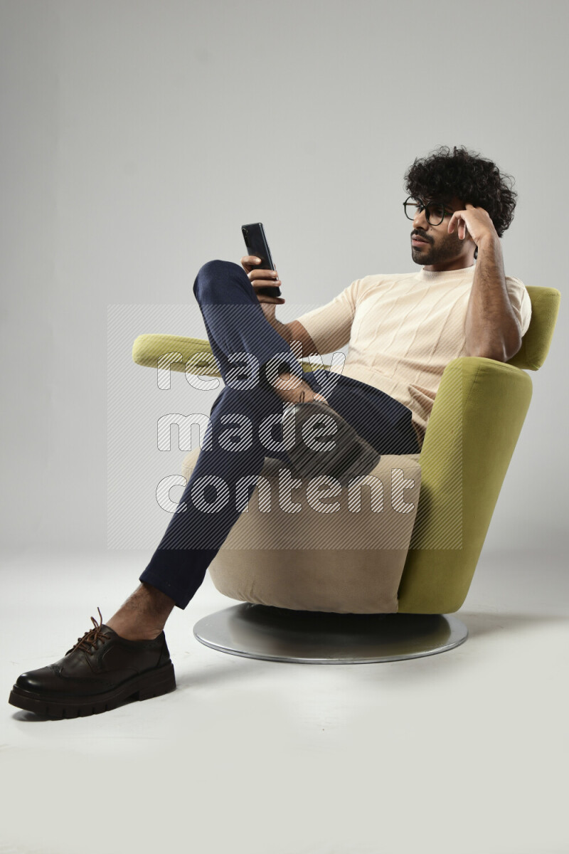 A man wearing casual sitting on a chair texting on the phone on white background