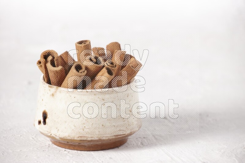 Cinnamon sticks in a beige bowl on a white background