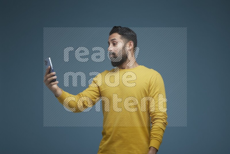 Man Taking a Selfie  in a blue background wearing a yellow shirt