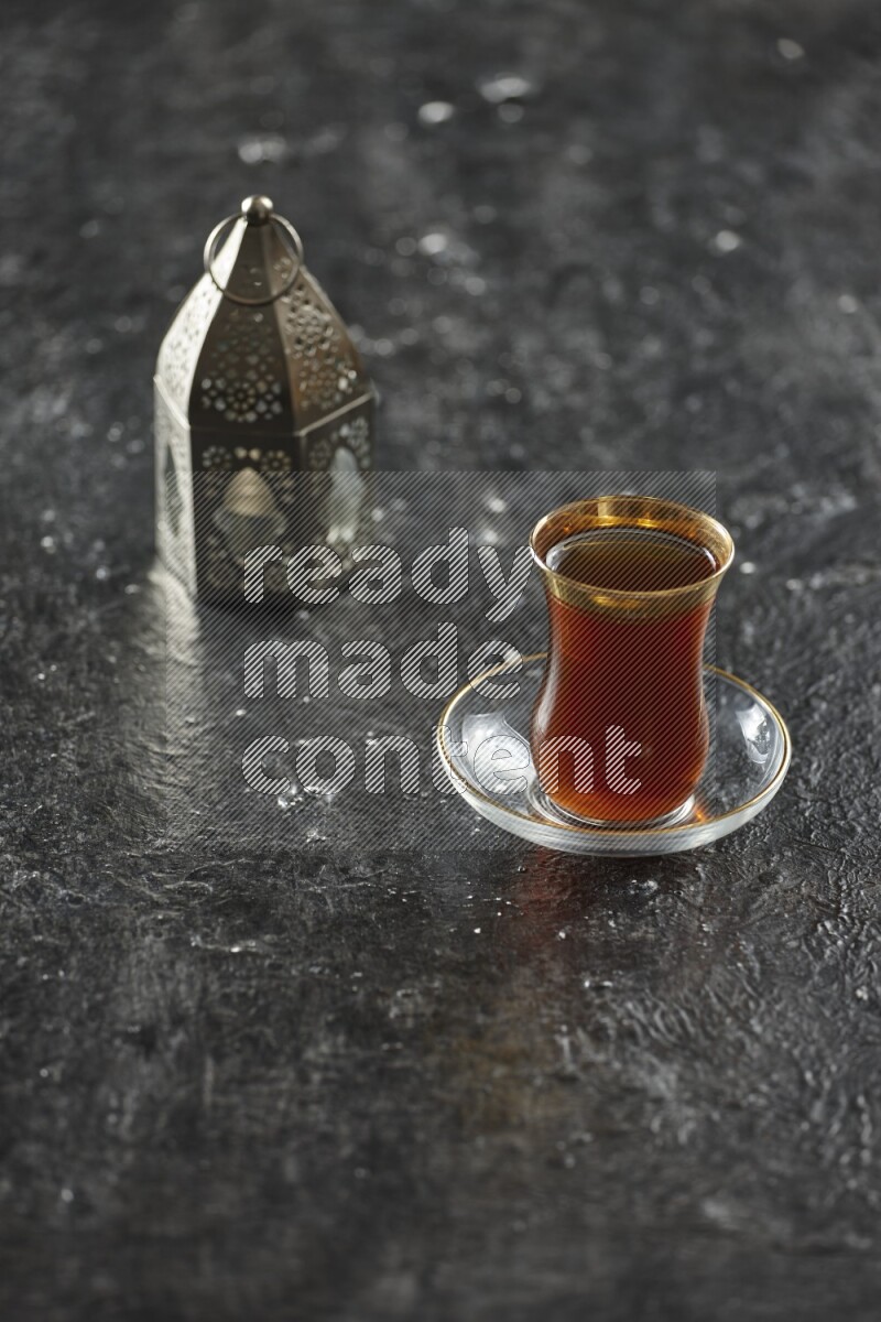 A silver lantern with different drinks, dates, nuts, prayer beads and quran on textured black background