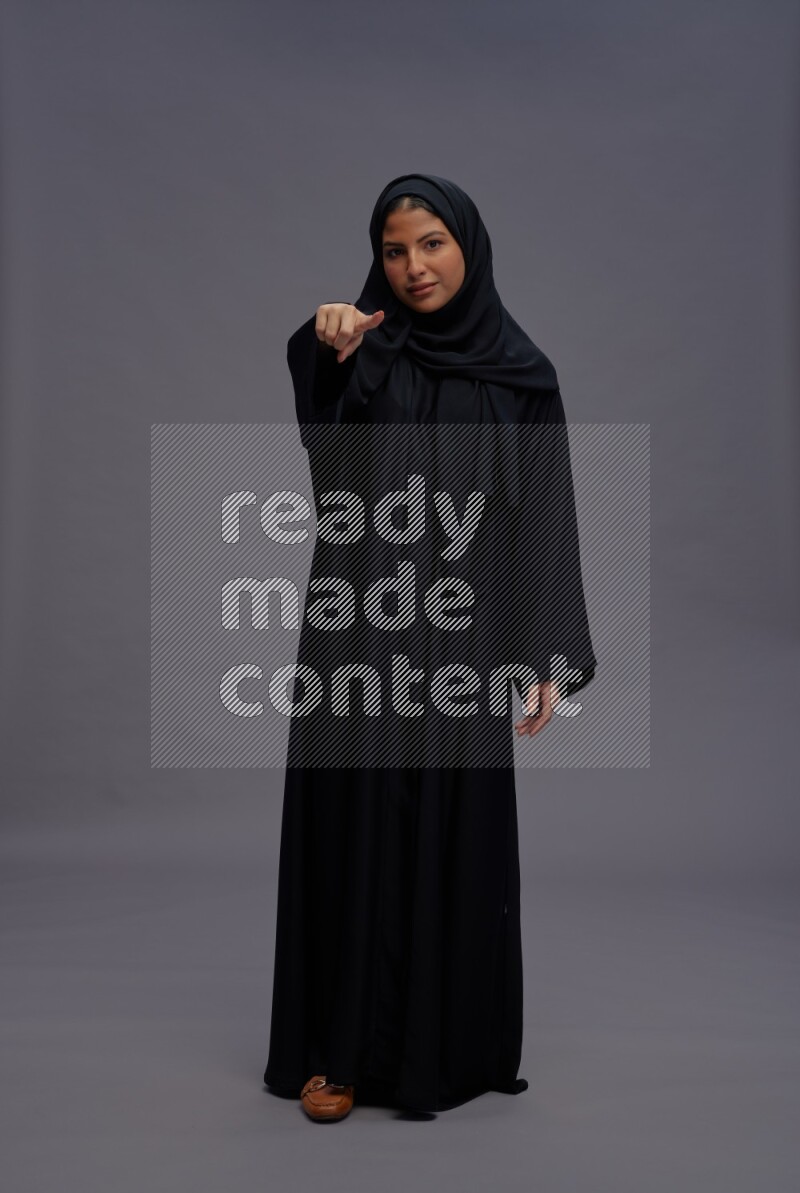 Saudi woman wearing Abaya standing interacting with the camera on gray background