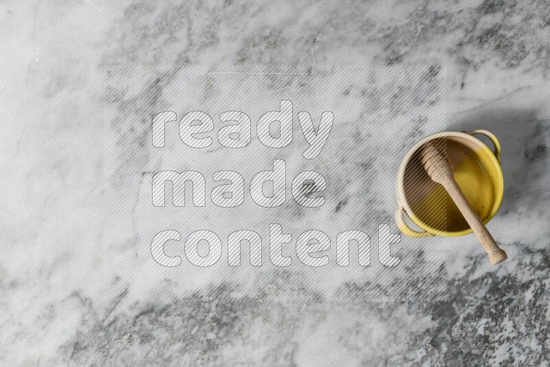 Multicolored pottery bowl with wooden honey dipper in it on grey marble background