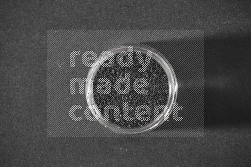 وعاء زجاجي ممتلئ ببذور حبة البركة علي خلفية سوداء