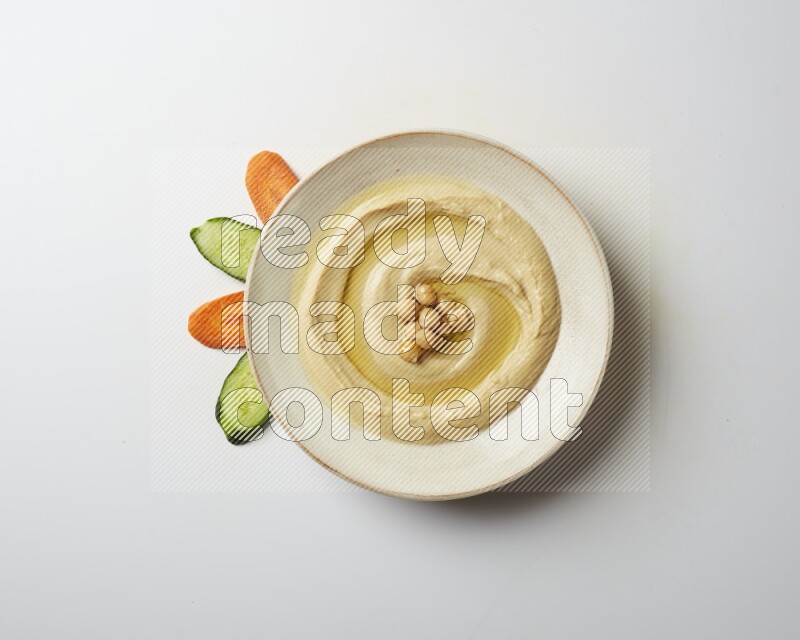 Hummus in a pottry plate garnished with roasted chickpeas on a white background