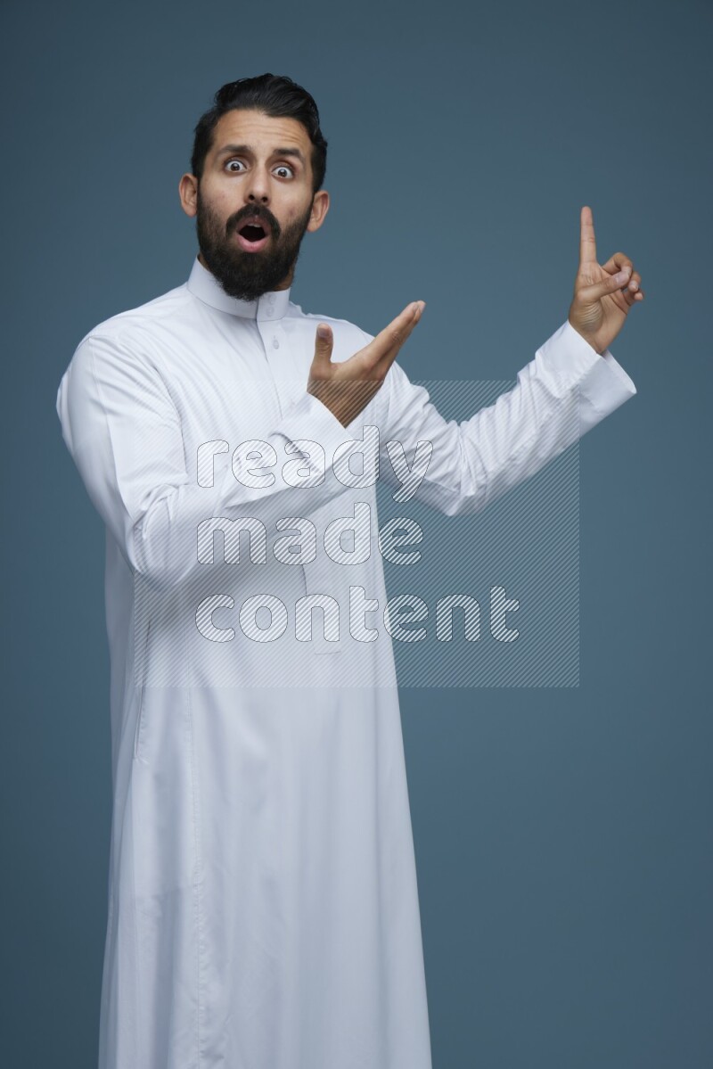 A man pointing in a blue background wearing Saudi Thob