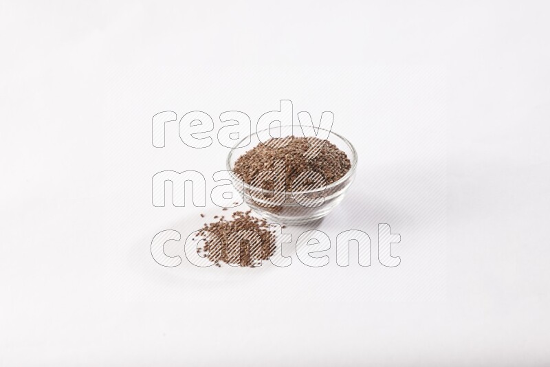 A glass bowl full of flax seeds surrounded by flax seeds on a white flooring