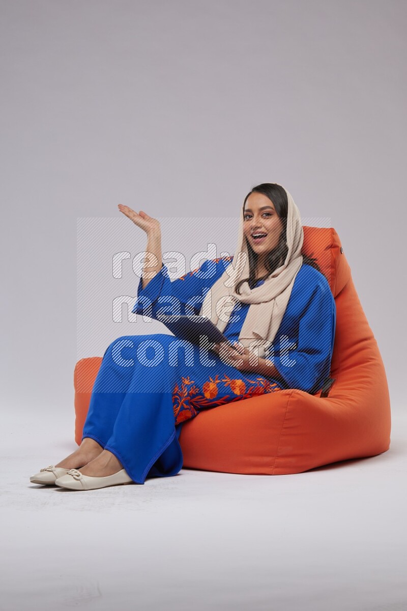 A Saudi woman sitting on an orange beanbag and working on tablet
