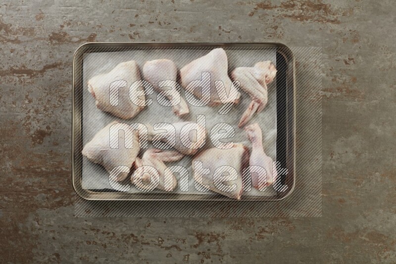 Mixed fresh chicken pieces in an oven tray on a textured rustic background