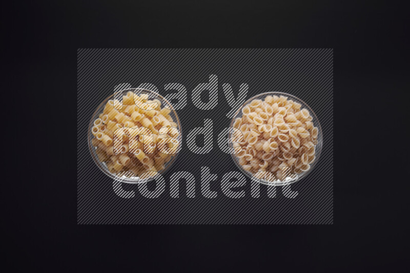 Different pasta types in glass bowls on black background