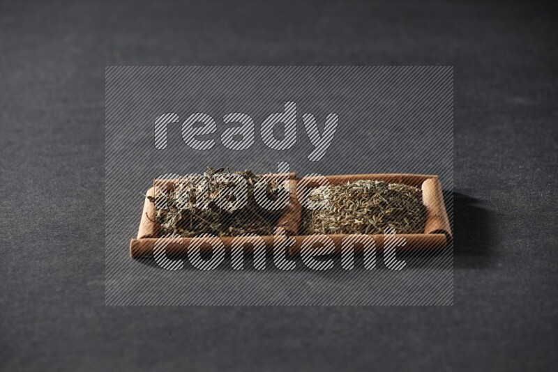 مربعان من أعواد القرفة ممتلئان بحبوب الكمون والريحان المجفف علي خلفية سوداء