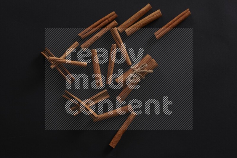 4 Cinnamon sticks stacked and bounded with more sticks in the background on black flooring