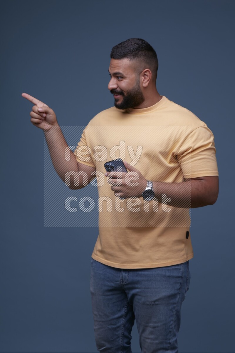 A man Pointing at a Smartphone on Blue Background wearing Orange T-shirt