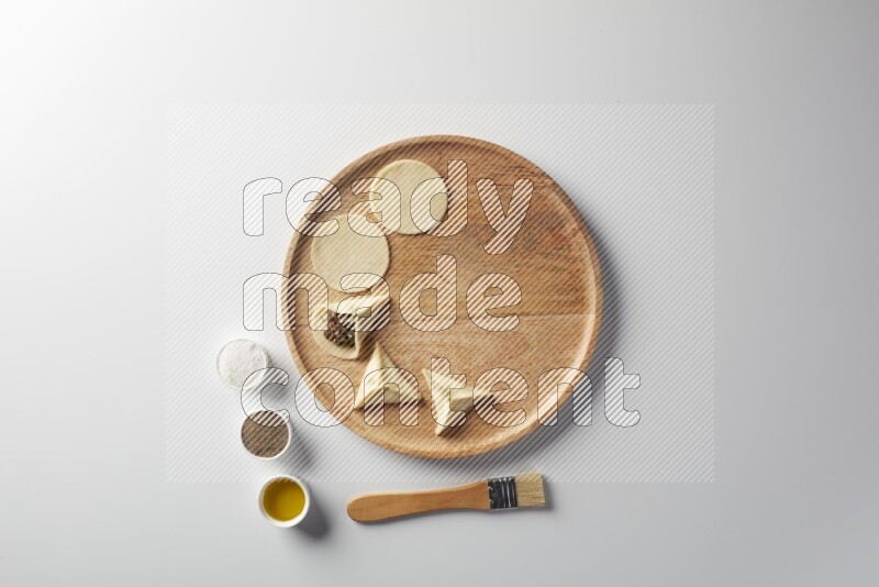 two closed sambosas and one open sambosa filled with meat while salt, black pepper and oil with oil brush aside in a wooden dish on a white background