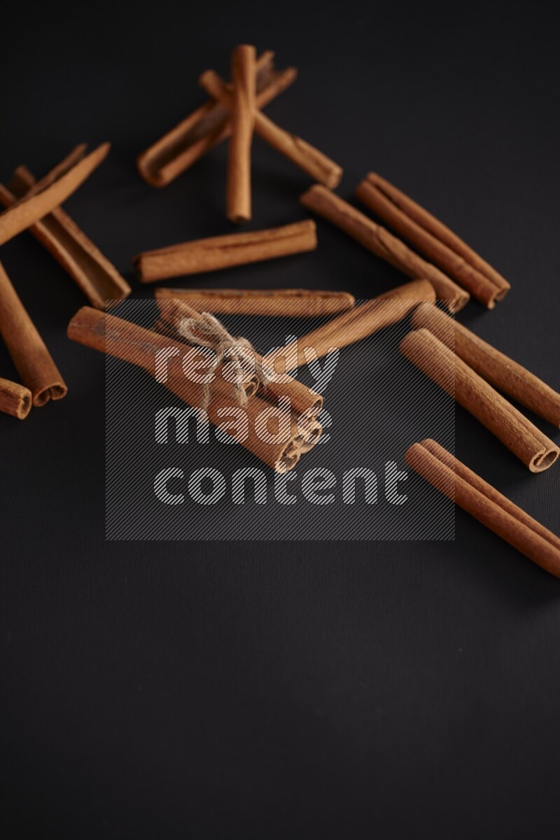 4 Cinnamon sticks stacked and bounded with more sticks in the background on black flooring